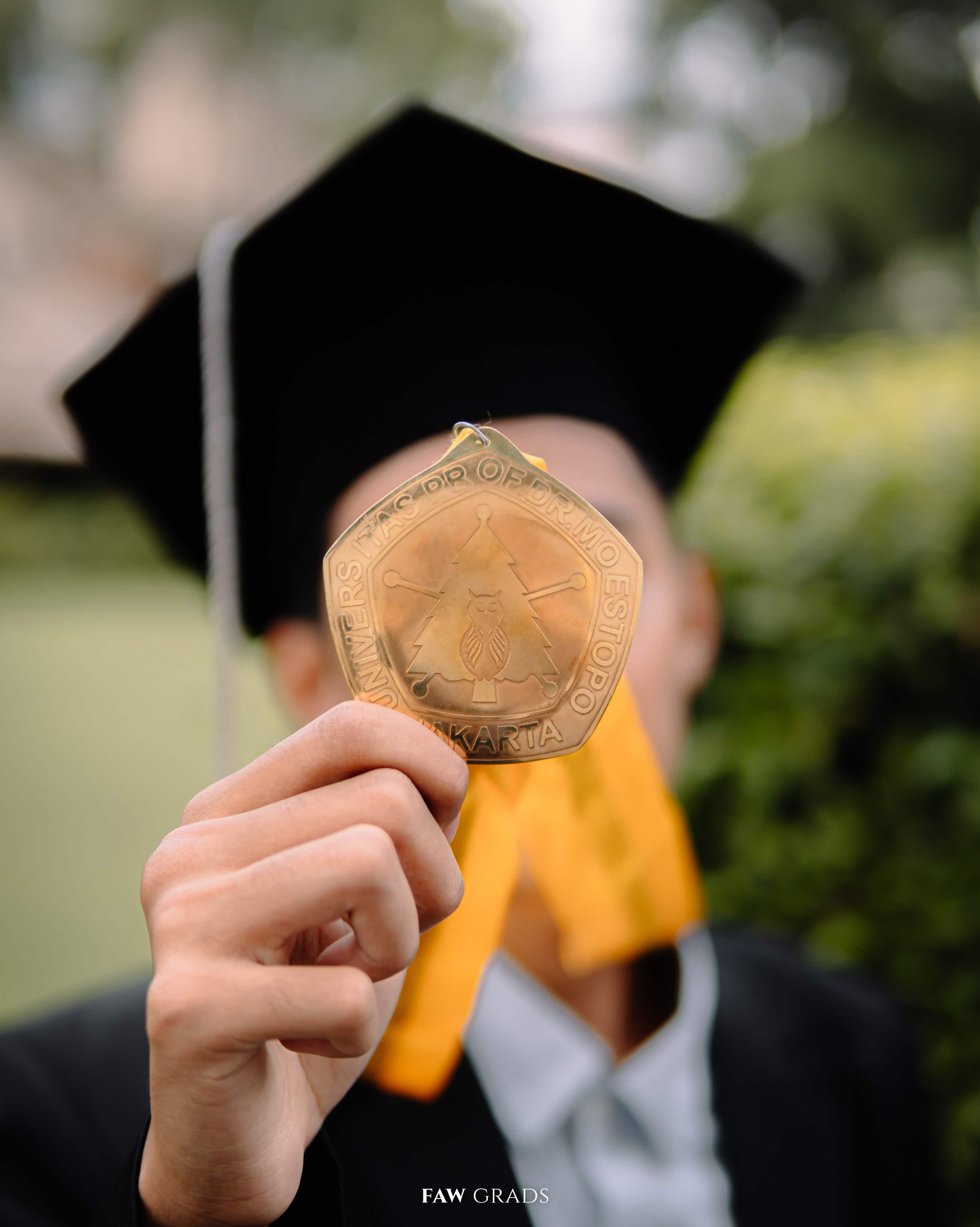 Black and white graduation portrait of an economics graduate lying on the grass, holding his cap